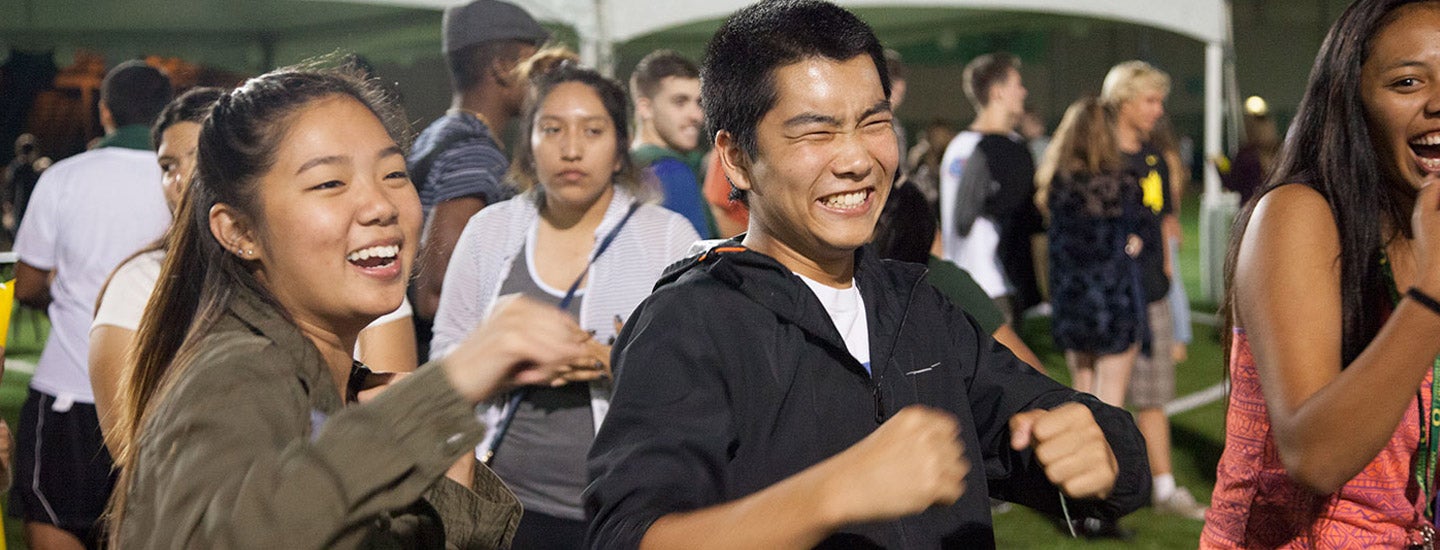 Excited crowds of students having a good time on the turf fields at night.